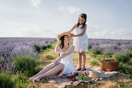 girl holding straw hat near happy mom sitting on blanket near fresh fruitsの写真素材
