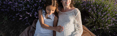 high angle view of happy pregnant woman in openwork dress near daughter in lavender field, bannerの写真素材