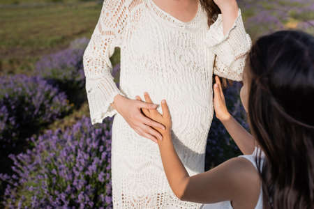 blurred girl hugging belly of pregnant mom in lavender meadow