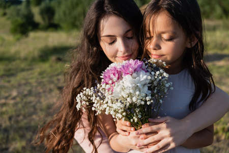 woman and girl with closed eyes smelling bouquet of aromatic flowersの写真素材