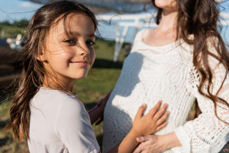 happy girl looking at camera near pregnant mom on blurred backgroundの写真素材