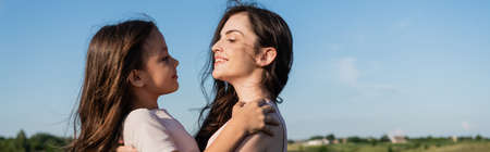 side view of happy brunette mother and daughter looking at each other outdoors, banner