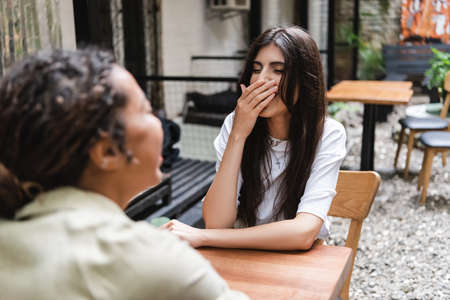 Cheerful woman laughing near blurred african american friend on cafe terraceの写真素材