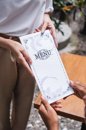 Cropped view of waitress holding menu near african american client on terrace of cafeの写真素材