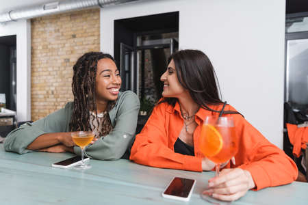 Multiethnic girlfriends talking near smartphones and cocktails in cafe