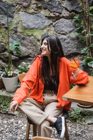 Smiling woman holding cocktail near table on terrace of cafeの写真素材