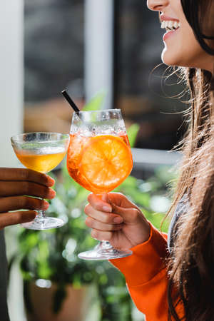Cropped view of cheerful woman toasting cocktail with african american friend in cafeの写真素材