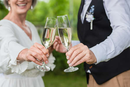 cropped view of happy and mature newlyweds clinking glasses of champagne in green gardenの写真素材