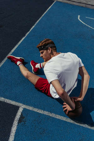top view of redhead basketball player sitting on court near ball