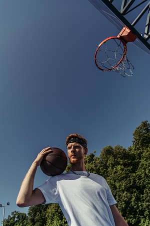 low angle view of sportive man standing with ball under basketball hoopの写真素材
