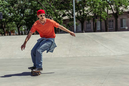 full length of man in orange t-shirt and red beanie riding in skate parkの写真素材