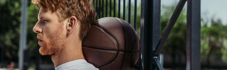 side view of basketball player with ball near fence, banner
