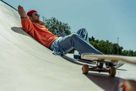 low angle view of happy and stylish man lying on ramp near blurred skateboardの写真素材