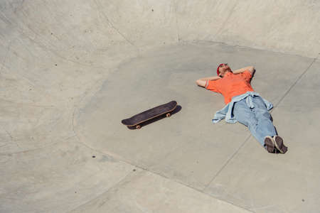 high angle view of trendy man lying near skateboard in skate parkの写真素材