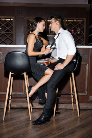 Side view of man holding glass of whiskey near seductive girlfriend in dress near barの写真素材