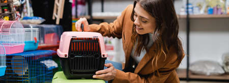 Brunette woman looking at animal cage in pet shop, banner