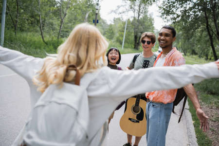 blurred woman with outstretched hands running towards happy multiethnic friends