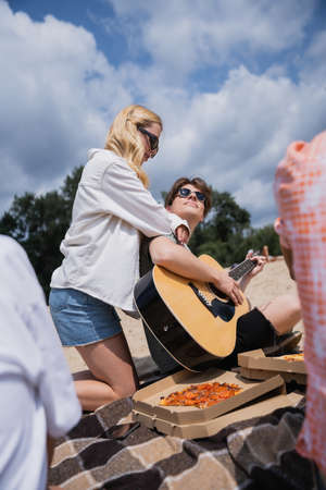 man playing guitar near blonde woman and friends during beach partyの写真素材