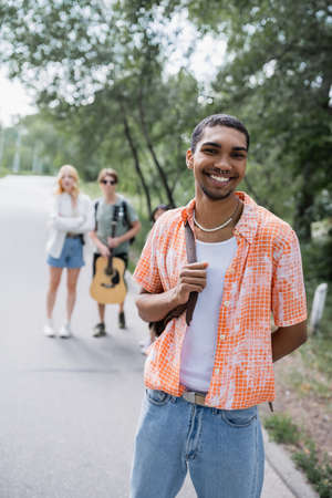 happy african american traveler looking at camera near friends on blurred road