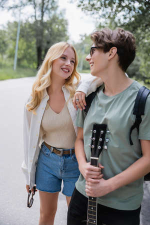 man with guitar and blonde woman smiling at each other while walking in countryside