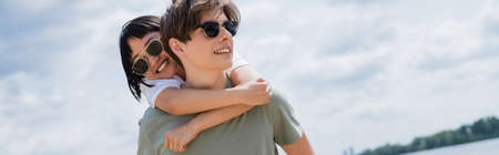 young man piggybacking asian woman in sunglasses, banner