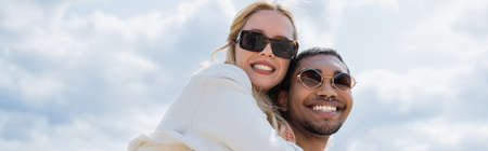 cheerful african american man in sunglasses piggybacking young girlfriend, banner