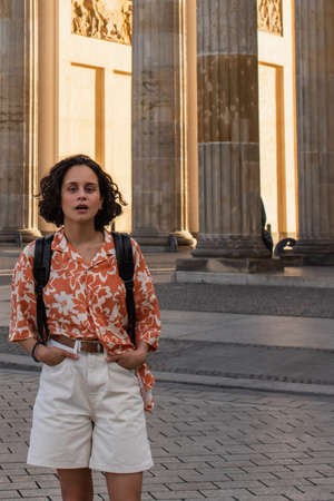 amazed traveler with backpack standing with hands in pockets near ancient columns