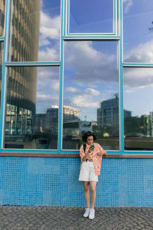 curly young woman chatting on smartphone near building in berlin