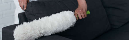 cropped view of housewife cleaning couch with dust brush, banner