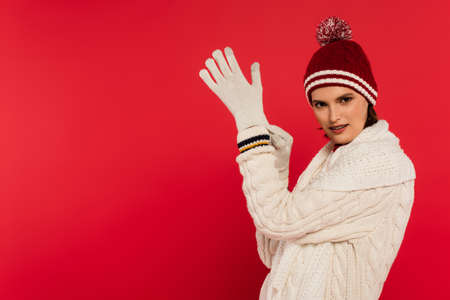 Smiling woman in warm clothes and hat wearing gloves isolated on redの写真素材