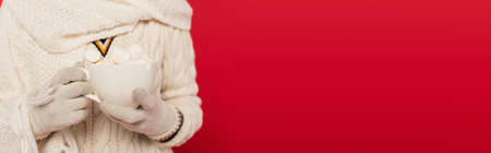 Cropped view of woman in knitted gloves and scarf holding cup with marshmallows isolated on red, bannerの写真素材