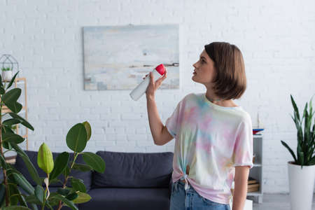 Side view of woman spraying air freshener in living roomの写真素材