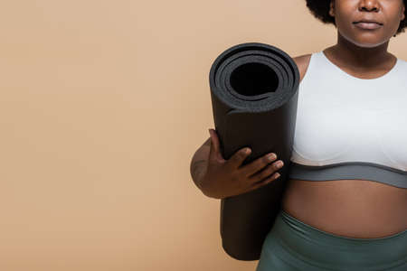 cropped view of african american plus size woman holding fitness mat isolated on beige