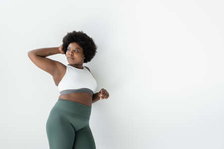 curly african american plus size woman in sportswear standing near white wallの写真素材