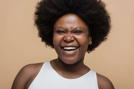 portrait of joyful african american plus size woman isolated on beigeの写真素材
