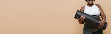 cropped view of happy african american plus size woman with tattoo holding fitness mat isolated on beige, bannerの写真素材