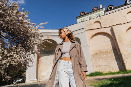 low angle view of african american woman in trendy outfit standing near blooming tree in pragueの写真素材