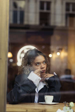 stylish african american woman eating foam from cappuccino cup in cafeの写真素材
