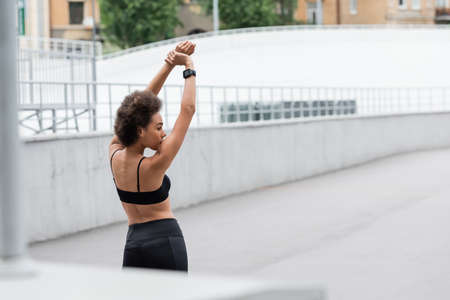 Side view of african american sportswoman in black top warming up on stadium at daytimeの写真素材