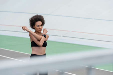 brunette african american woman in black sports bra stretching arms on blurred foreground