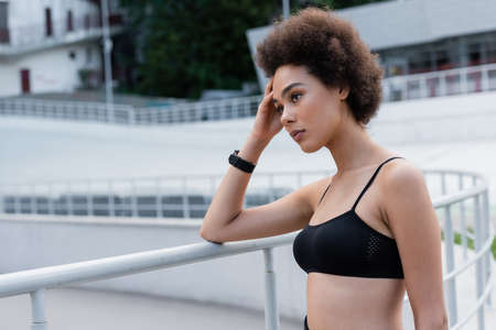 pensive african american sportswoman holding hand near head and looking away outdoors