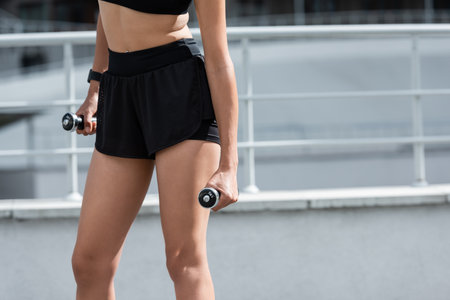 Cropped view of fit african american sportswoman holding dumbbells on stadiumの写真素材