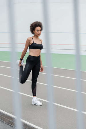 full length of sportive african american woman stretching on blurred foreground