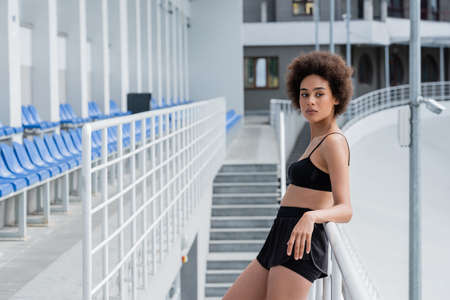 Fit african american sportswoman in black sportswear standing near railing on stadium