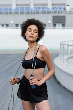 Portrait of african american sportswoman holding jump rope and looking at camera on stadiumの写真素材