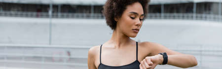 Young african american sportswoman looking at smart watch on stadium, bannerの写真素材