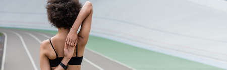 Back view of african american sportswoman warming up on blurred stadium, bannerの写真素材