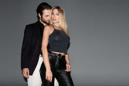 Young man kissing stylish blonde girlfriend on grey background