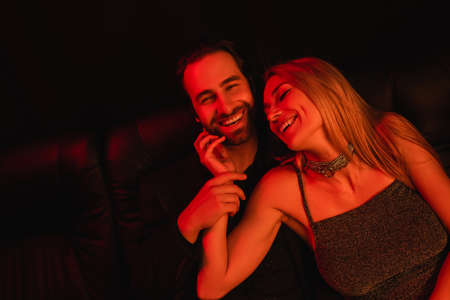 Smiling woman touching bearded boyfriend in red lighting on black backgroundの写真素材