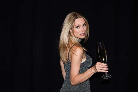 Stylish woman in dress holding glass of champagne during party isolated on black